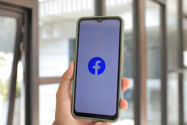 Close-up of smartphone with Facebook app open held by hand indoors. Facebook Shops vs TikTok Shop UK: checkout and VAT compared