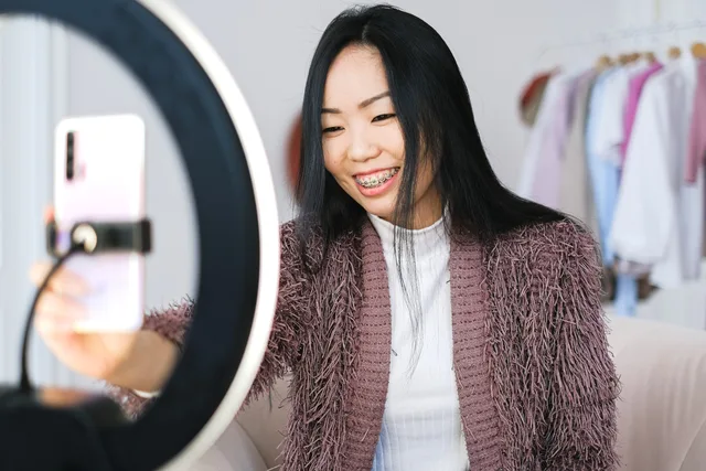 Smiling woman using smartphone and ring light for live streaming indoors. Live shopping platforms UK: best options for retailers