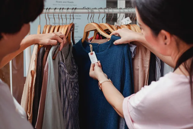 Two women browse clothes in a boutique, examining a blue dress. Where AI belongs in a social commerce operation, starting with catalogue exception triage