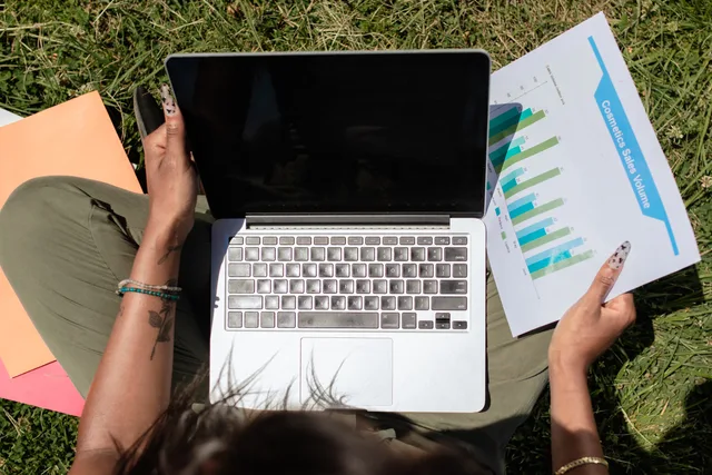 Woman reviewing sales charts on a laptop while sitting on grass, showcasing remote work flexibility. Social commerce analytics tools UK: measure your sales