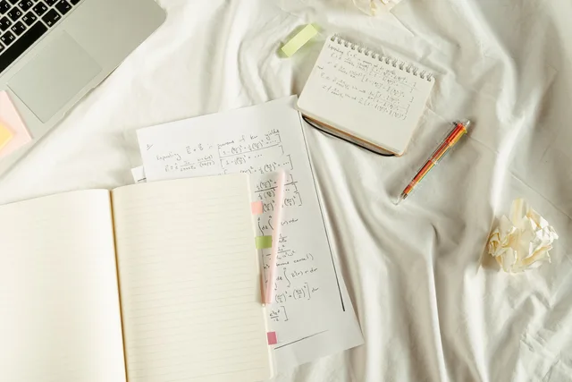 Flat lay of a cozy study space with notebooks, math formulas, and laptop on bed. Platform, last-touch, promo code or multi-touch? Social commerce attribution compared