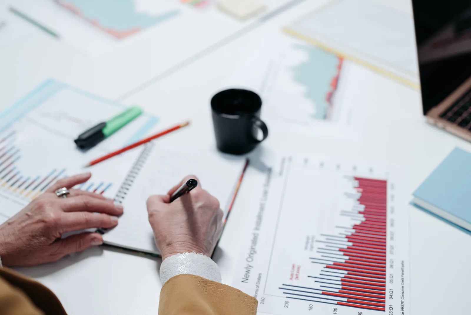 Close-up of hands writing in a notebook surrounded by business charts and documents.