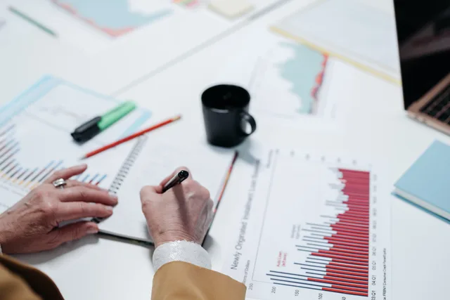 Close-up of hands writing in a notebook surrounded by business charts and documents. Checking a social commerce benchmark for comparability before it becomes a target