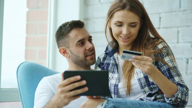 Young couple sitting indoors, shopping online with a tablet and credit card. Social commerce personas organised around buying tasks and checkout doubts