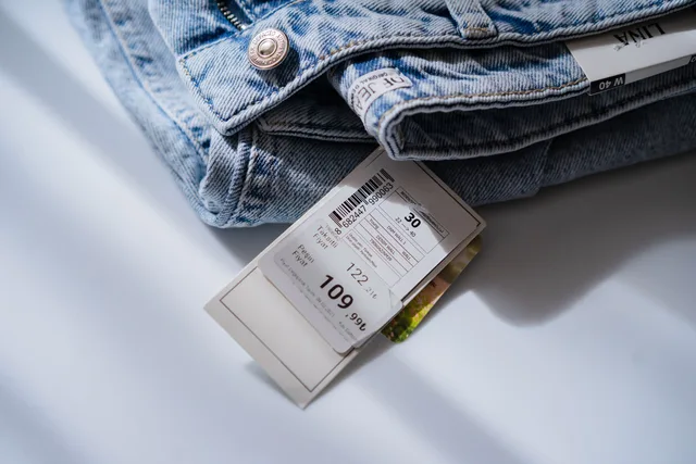 From above of blue jeans with retail price and size label placed on white table. Cardiff social commerce: Welsh-English listings side by side