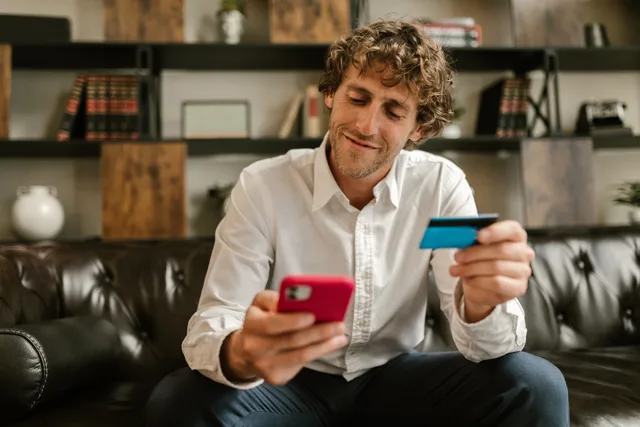 Caucasian man using smartphone and credit card for online shopping indoors. How to compare social commerce routes and agencies on transaction evidence