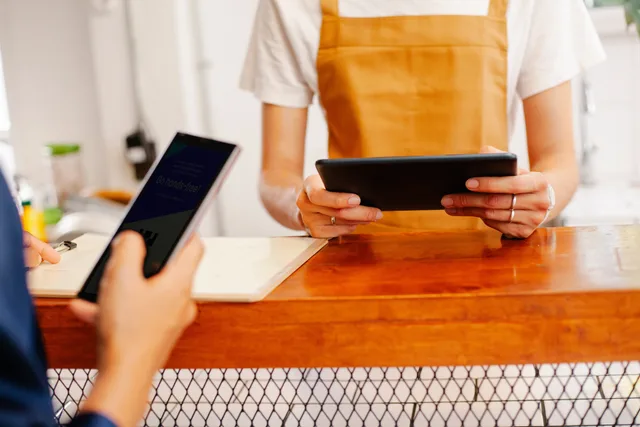 Crop anonymous female colleagues surfing internet on cellphone with black screen and tablet in cafe. Social commerce software selection: pass/fail tests