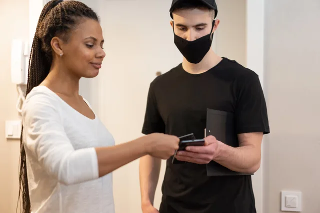 Woman using smartphone for cashless payment with delivery person at home. Choosing social commerce tools by starting with the route a customer will take